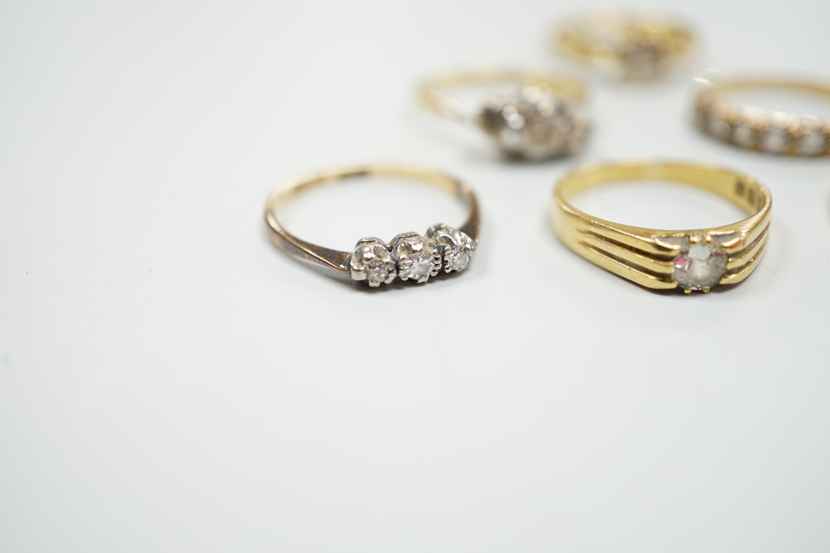 Six assorted gold dress rings, comprising an 18ct gold and platinum three stone ring, size O, an 18ct gold claw set solitaire diamond ring, size O, an 18ct gold illusion set solitaire diamond ring, size L, an 18ct gold t